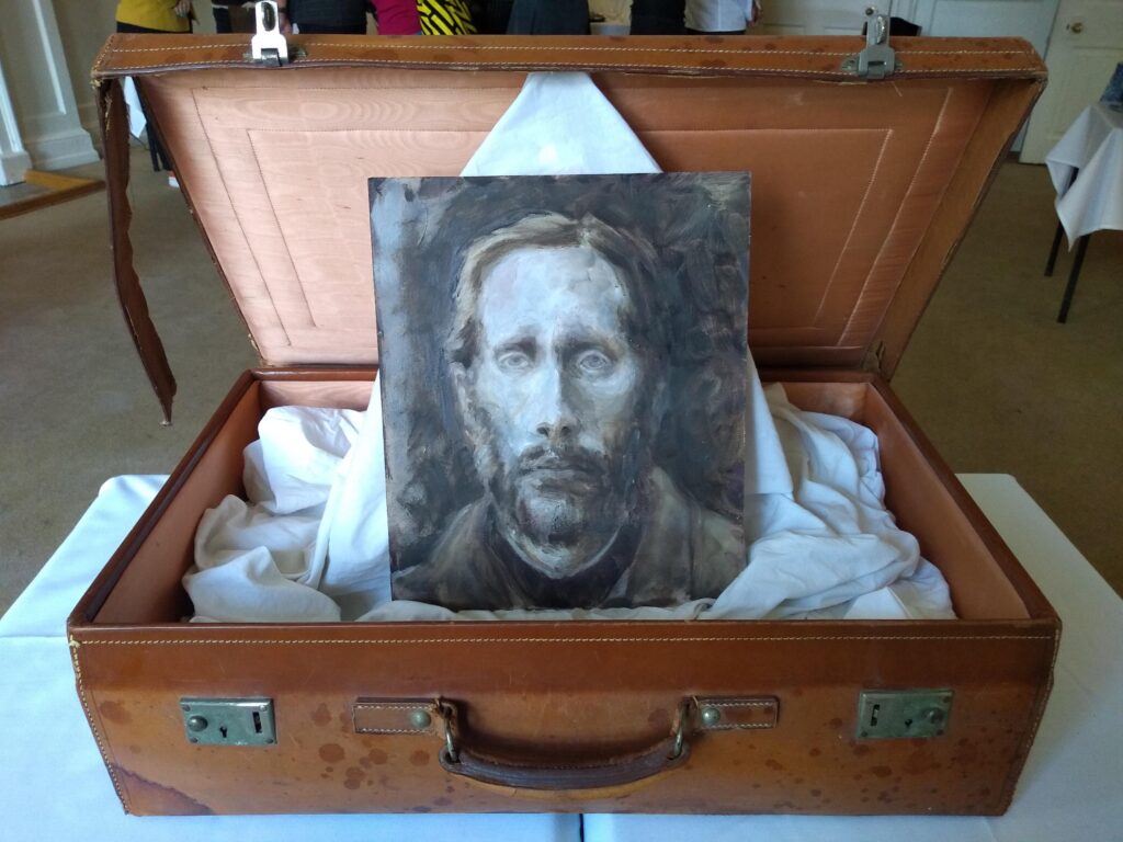 A suitcase with a portrait of a bearded individual from the County Asylum.
